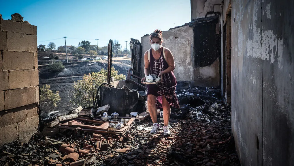 Μια γυναίκα σε απόγνωση μαζεύει μέσα από τα αποκαΐδια του σπιτιού της στο Κρυονέρι Αττικής κάποια σερβίτσια που σώθηκαν. 