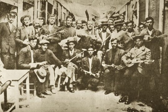 Ρεμπέτες στον Πειραιά το 1933. Ο Βαμβακάρης διακρίνεται όρθιος αριστερά κρατώντας μπουζούκι