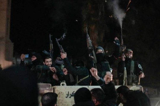 members of the new security forces, primarily fighters from Hayat Tahrir al-Sham (HTS), fire into the air in celebration in Homs, Syria