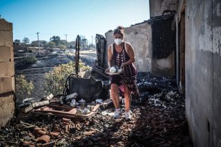 Μια γυναίκα σε απόγνωση μαζεύει μέσα από τα αποκαΐδια του σπιτιού της στο Κρυονέρι Αττικής κάποια σερβίτσια που σώθηκαν.