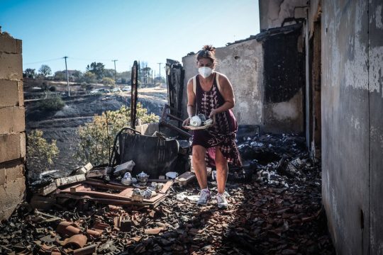 Μια γυναίκα σε απόγνωση μαζεύει μέσα από τα αποκαΐδια του σπιτιού της στο Κρυονέρι Αττικής κάποια σερβίτσια που σώθηκαν.