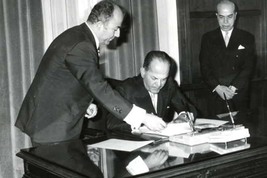 8 Οκτωβρίου 1973. Ο Μαρκεζίνης παρακολουθεί υπομονετικά την προσυπογραφή του πρακτικού της ορκωμοσίας του ως «δοτού» πρωθυπουργού από τον δικτάτορα Παπαδόπουλο