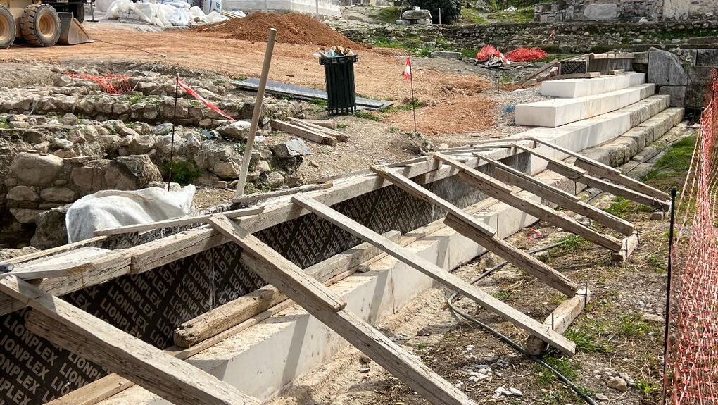 Αποψη βαθμίδων της ρωμαϊκής περιόδου, από πωρόλιθο, που διαμόρφωναν το δυτικό όριο της διεύρυνσης της Παναθηναϊκής οδού προς τα δυτικά. Επέτρεπαν την πρόσβαση στη χαμηλότερη στάθμη ανάμεσα στην Παναθηναϊκή οδό και στο ανατολικό άκρο της Μέσης Στοάς. Επάνω στις αυθεντικές βαθμίδες κατασκευάζονται επιτόπου νέες από μπετόν αρμέ, αναπαράγοντας τη μορφή του αρχαίου οικοδομήματος. Μάρτιος 2026