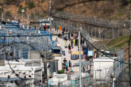 Οι μετανάστες στο προαύλιο της δομής, περιστοιχισμένοι από συρματοπλέγματα που παραπέμπουν σε φυλακές υψίστης ασφαλείας